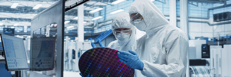 Lab technicians in cleanroom suits inspecting a silicon transistor wafer.