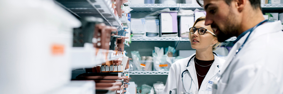 Two pharmaceutical technicians take stock of medications on a shelf.