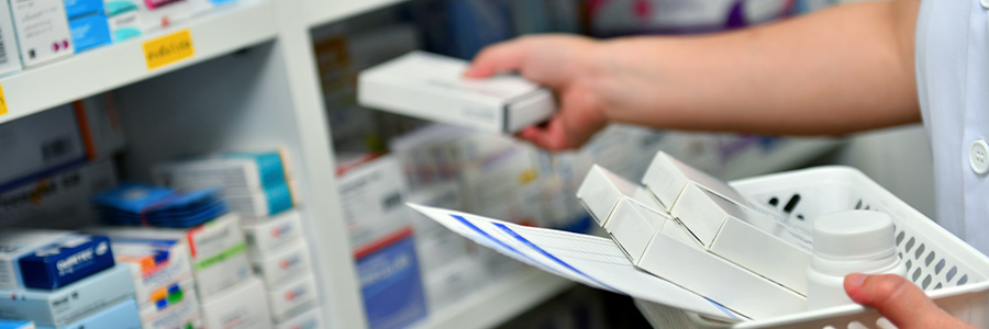 Gros plan des mains d’un pharmacien qui ramasse des ordonnances sur des étagères de médicaments emballés.