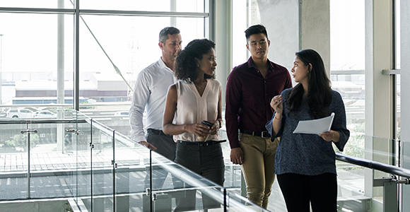 Groupe de collègues en pleine discussion déambulant dans les couloirs de l’entreprise.