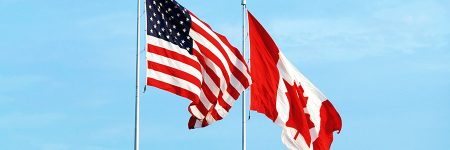 Les drapeaux américain et canadien flottent ensemble dans un ciel bleu.