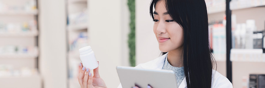 Un pharmacien tient une tablette et regarde une bouteille de médicaments sur ordonnance.