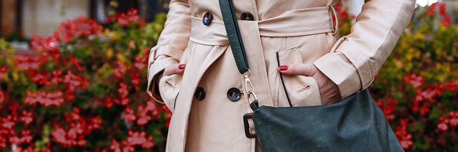 Mid-shot of a person wearing a stylish, beige trench coat with a belted waist, carrying a shoulder bag.