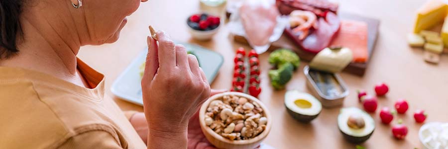 Une personne qui mange des noix, entourée d’aliments sains et frais sur une table.