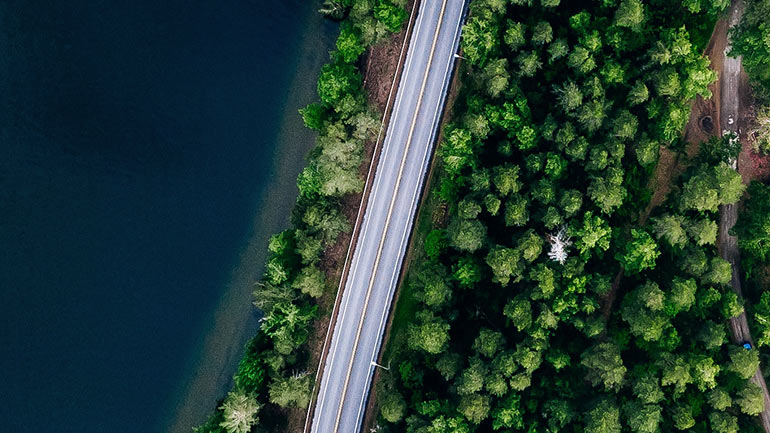 Satellite view of a road with a lake on one side and a forest on the other.