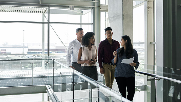 Groupe de collègues en pleine discussion déambulant dans les couloirs de l’entreprise.