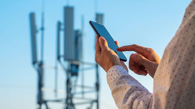 A person using a smartphone with cell towers in the background.