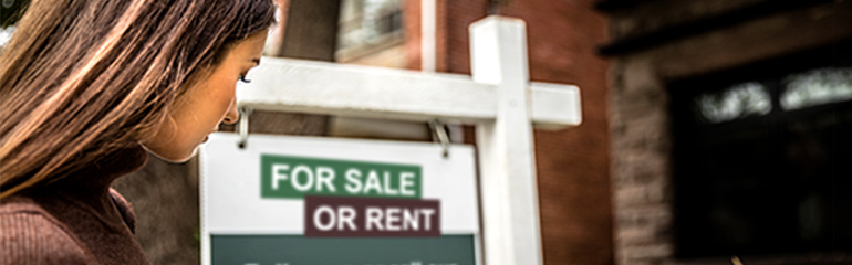 Woman looking over at a house for-sale or rent sign